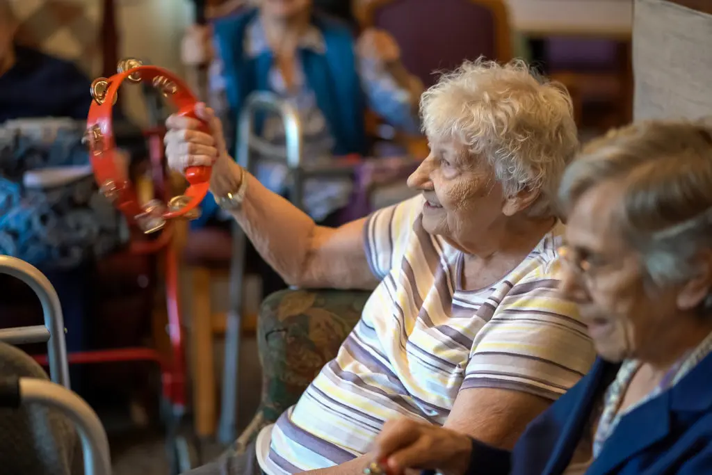 Elderly women participating in a music activity with tambourines at a senior respite care facility