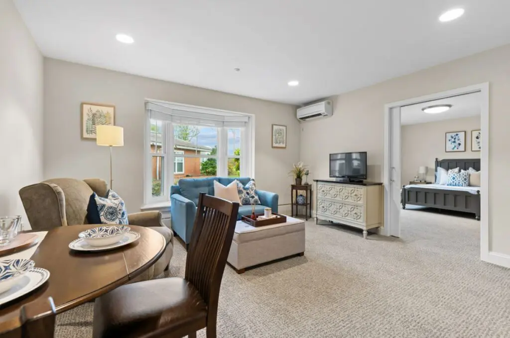 A bright, spacious one-bedroom apartment with a small table, loveseat and television at The Willows of Living Branches