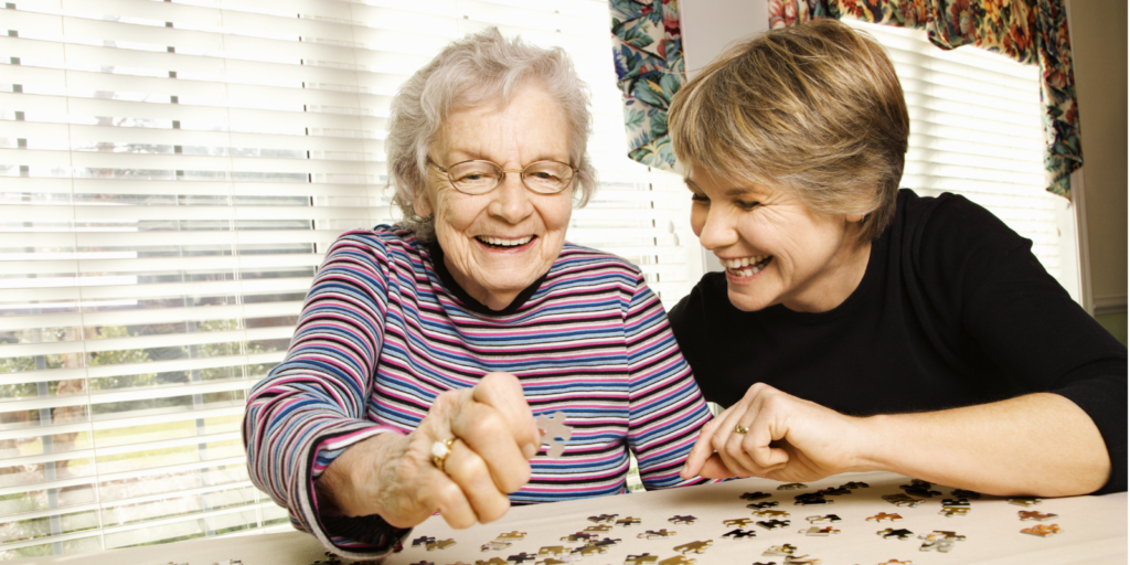 A young woman works on a puzzle with her senior mother in a memory care community